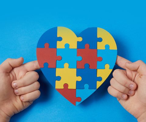 Autistic boy hands holding jigsaw puzzle heart shape. Autism spectrum disorder family support concept. World Autism Awareness Day.